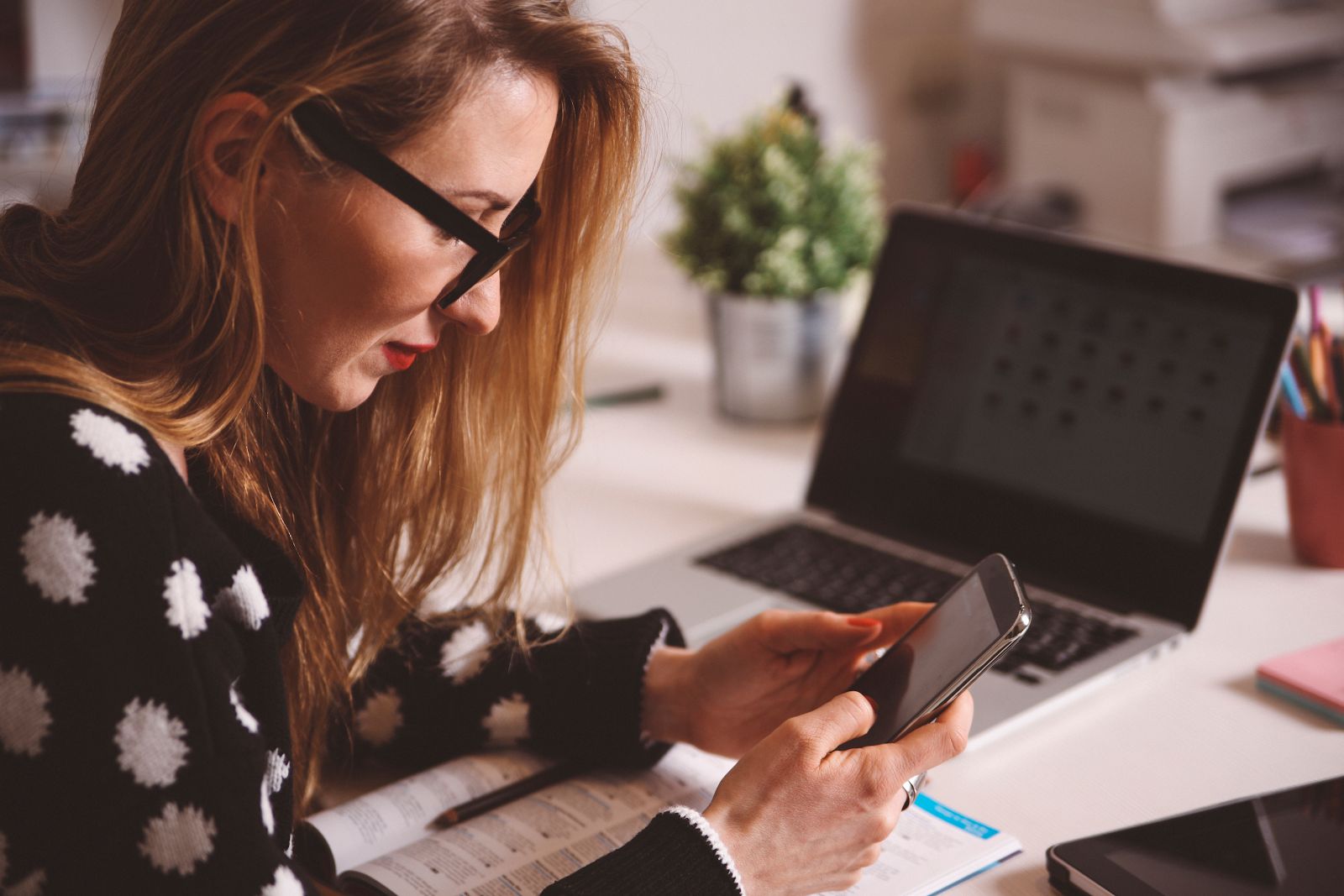 Woman with red hair and glasses uses her phone to work on her Instagram social media strategy.